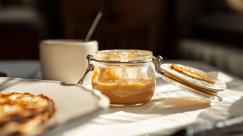 A half empty glass jar of peanut butter, on a table in the sunlight