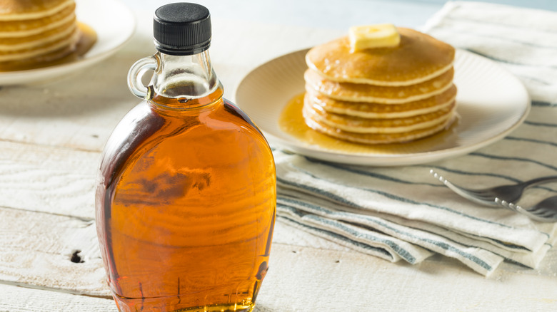 a bottle of maple syrup in front of a stack of pancakes