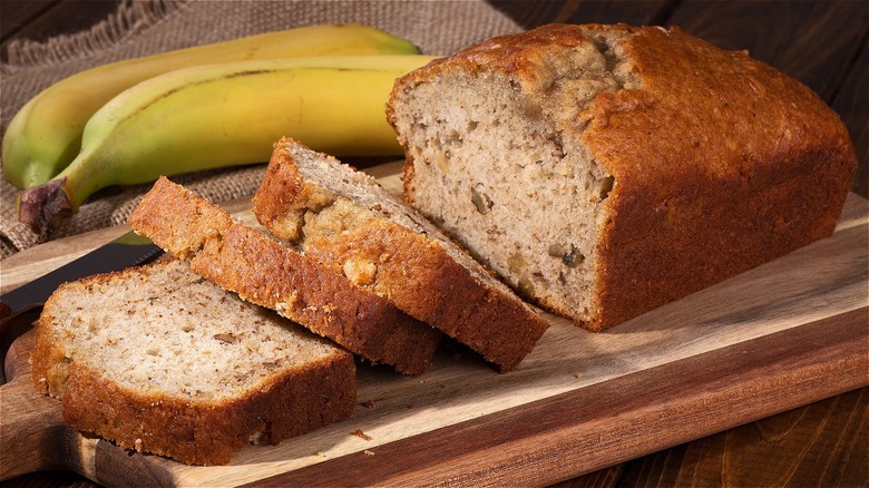 A loaf f banana bread over a wooden board next to bananas