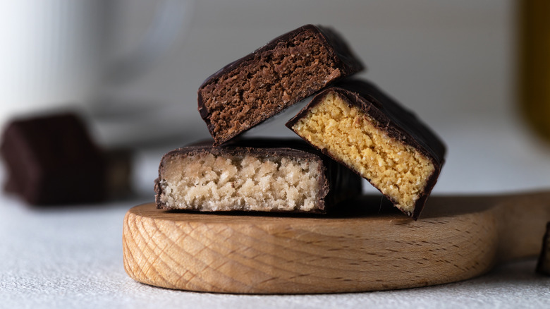 Various flavors of protein bars cut in half and stacked on top of each other on a wooden cutting board.