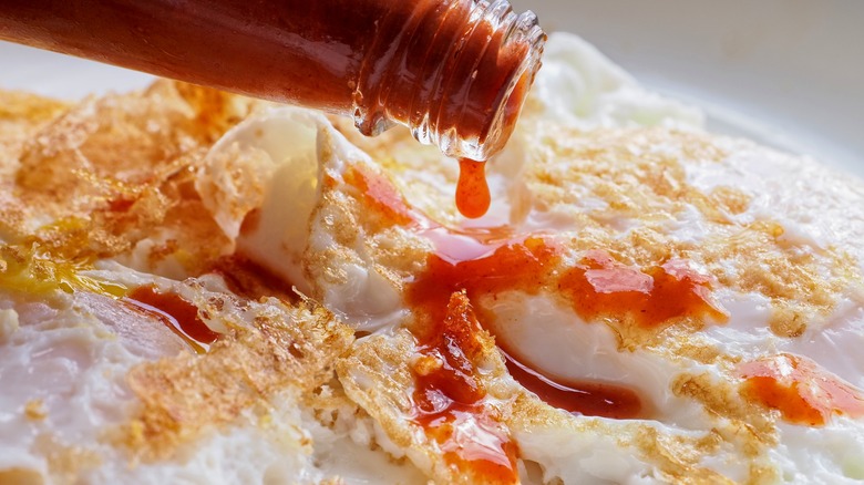 Close-up of hot sauce bottle pouring on fried eggs.