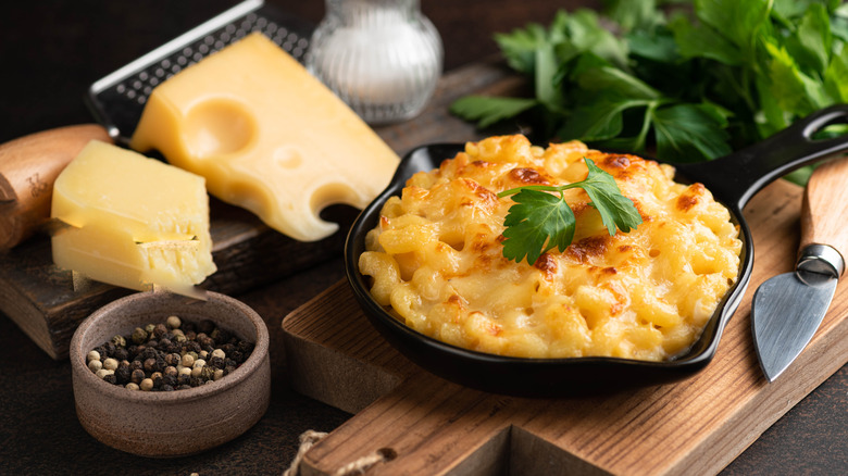Skillet of mac and cheese surrounded by fresh herbs and blocks of cheese