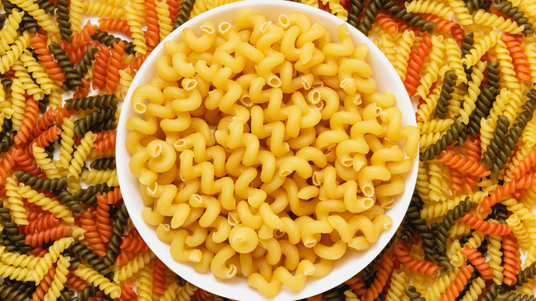Bowl of raw cavatappi noodles surrounded by fusilli noodles