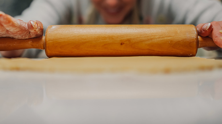 Hands rolling out dough on a shiny surface