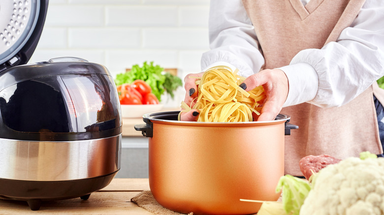Woman placing uncooked pasta in slow cooker