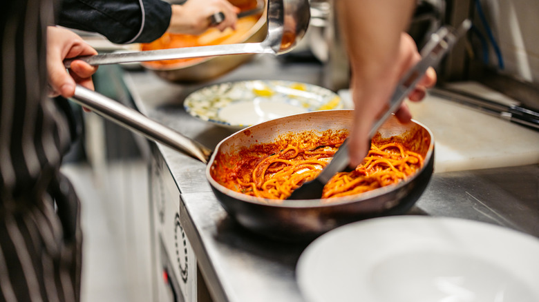 Spaghetti noodles being finish in the sauce in a pan