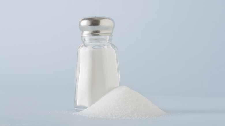 Shaker of salt behind a pile of salt on a light blue background