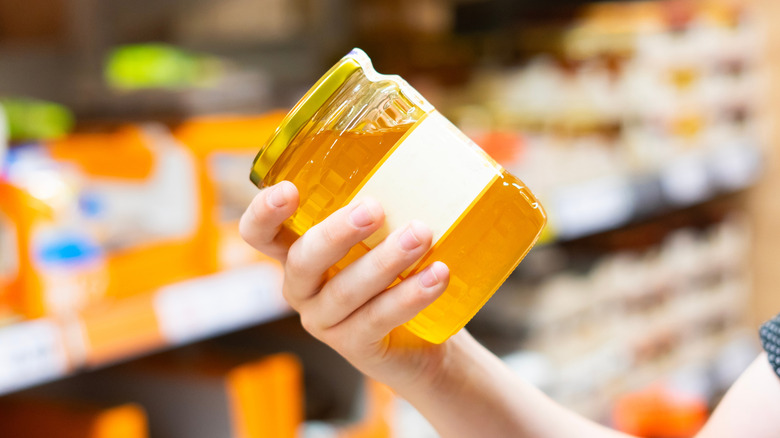 Hand holding jar of honey in supermarket