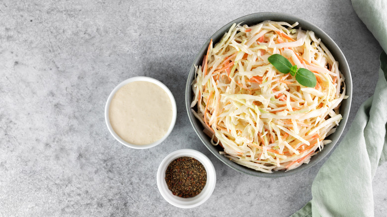 Coleslaw ingredients in a bowl with dressing and seasonings on the side