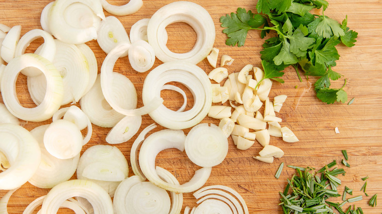 Sliced onions, garlic, and herbs on wooden cutting board