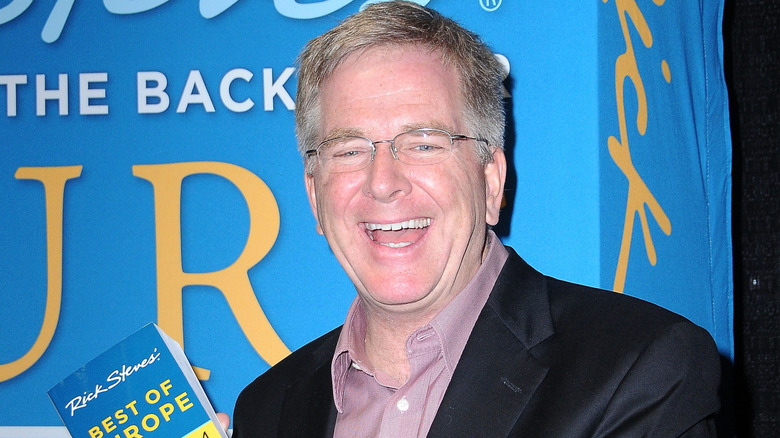 Rick Steves smiling and holding his book