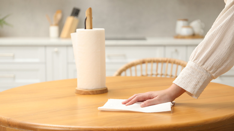 Hand wiping a paper towel on a table next to a roll of paper towels