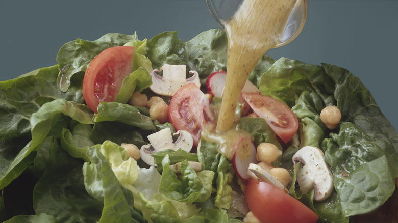 1970s photo of brownish dressing being poured on a green salad with mixed vegetables