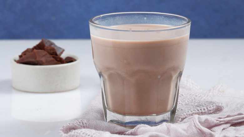 glass of chocolate milk next to ramekin of chocolate pieces