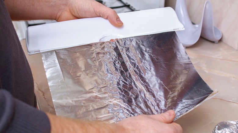 hands tearing sheet of aluminum foil