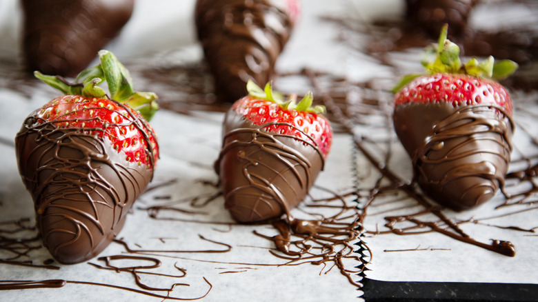 Strawberries dipped in and drizzled with tempered chocolate sitting on parchment paper