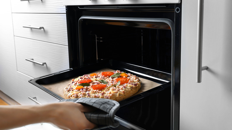 person putting sheet pan pizza in oven