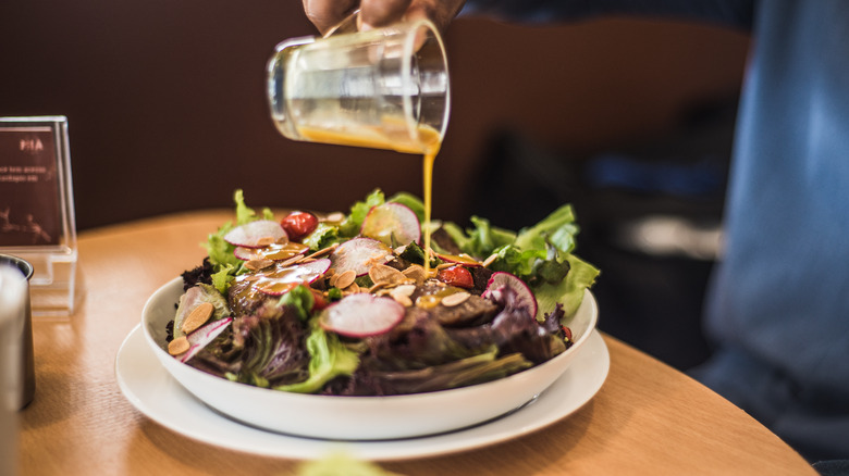 Person pouring vinaigrette over salad