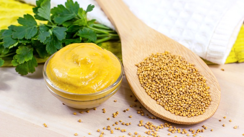 Yellow mustard in a dish and mustard seeds on a wooden spoon