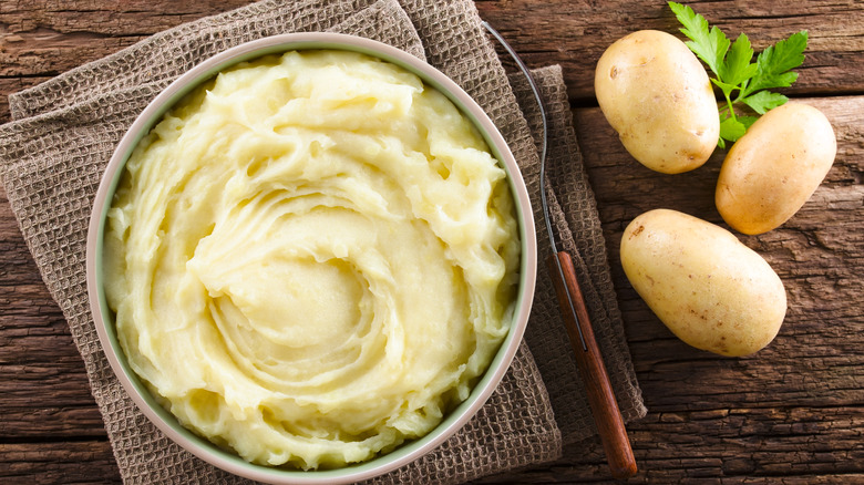 mashed potatoes in a bowl beside whole raw potatoes