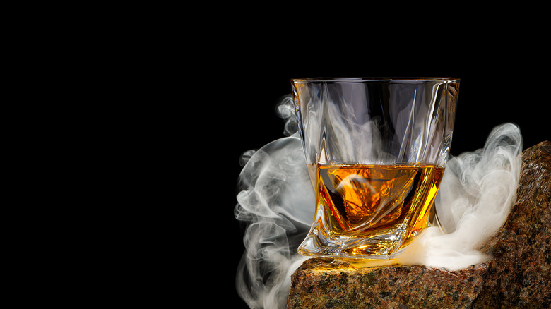 Whiskey glass on rock ledge surrounded by curling smoke