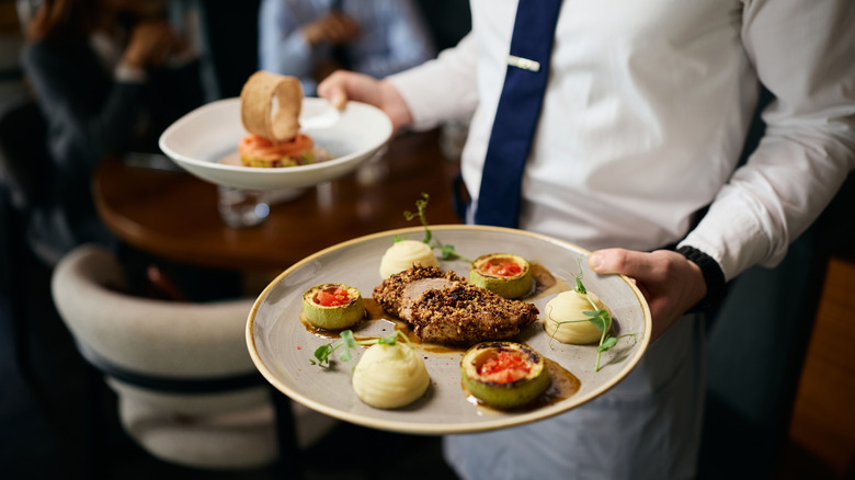 Restaurant server holding two plates of fine dining food