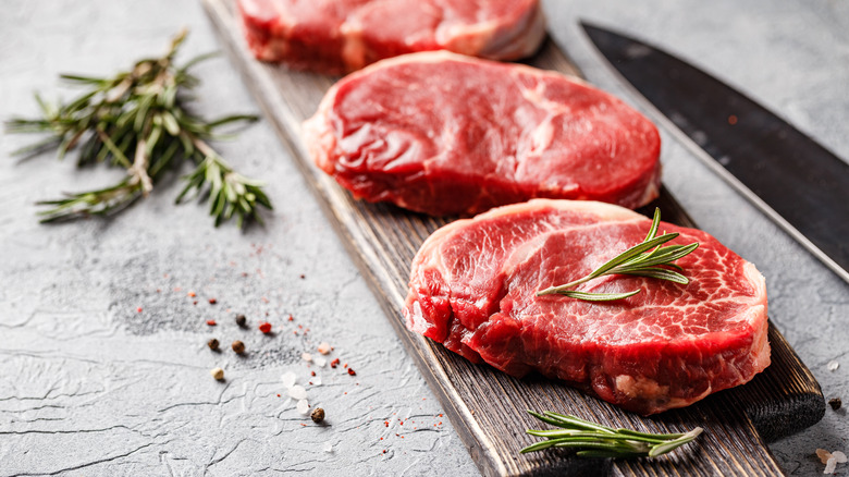 raw steaks on cutting board with rosemary sprigs