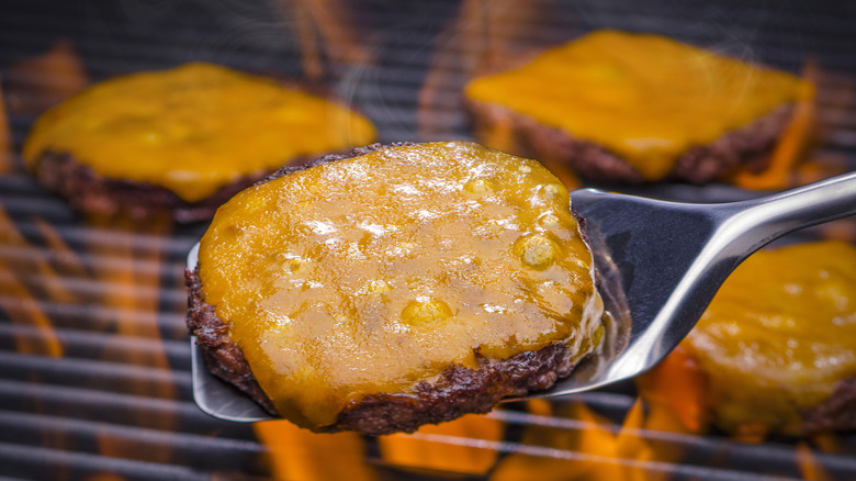 Cheeseburger on a spatula over a grill with other cheeseburgers on it.