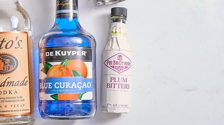Bottle of plum bitters sitting next to other cocktail ingredients