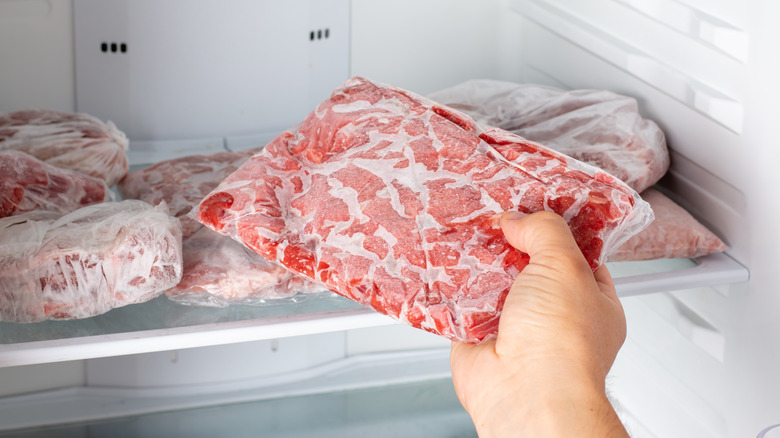 A hand grabbing frozen meat out of the freezer