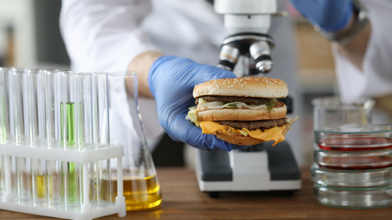 Scientist holding burger in lab with microscope and test tubes