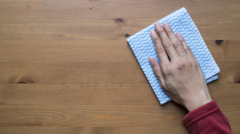 Hand cleaning wooden table with cloth