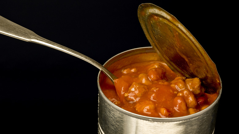 A spoon dipping into a partially open can of chili.