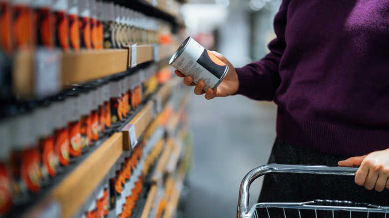 A person in a grocery store aisle examines a can of food.