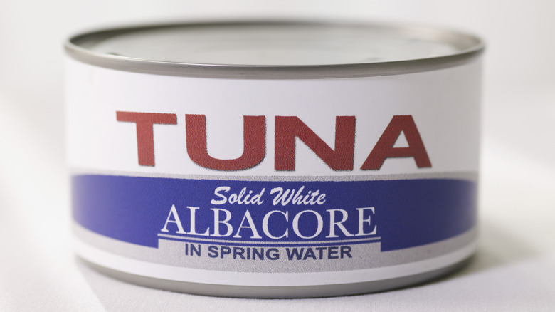 An unopened can of albacore tuna in water against a white background.