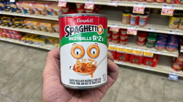 A can of SpaghettiOs with meatballs being held up in a grocery store aisle.
