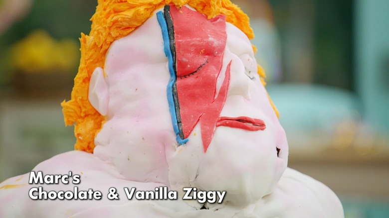 A cake bust of David Bowie as Ziggy Stardust, with a lumpy pink head, orange hair, and a misshapen lightning bolt