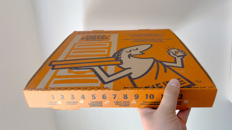 A person holding an orange Little Caesars pizza box against a white background