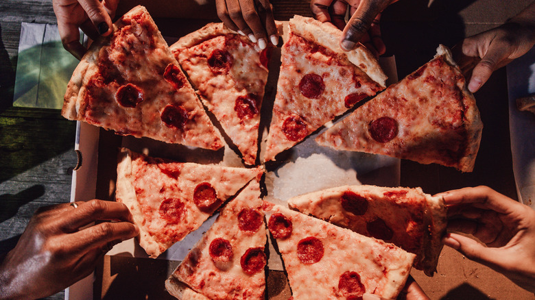 Top-down view of hands grabbing slices of pepperoni pizza