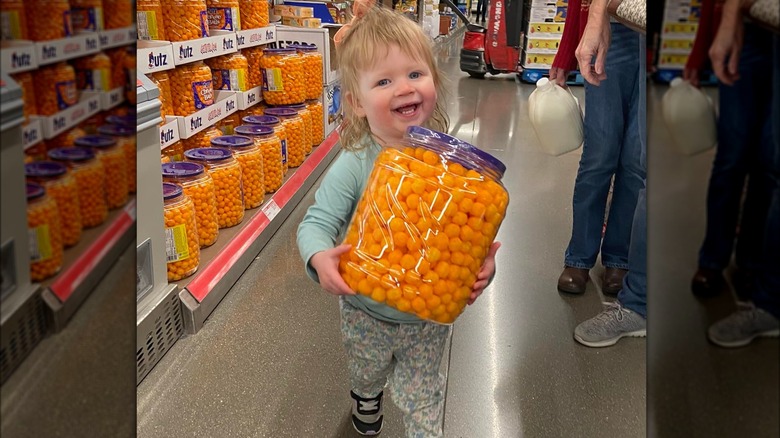 happy child with large container of cheeseballs in aldi store aisle