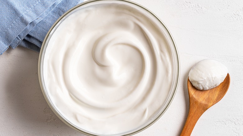 Dish of plain Greek Yogurt with a wood spoon on a white table