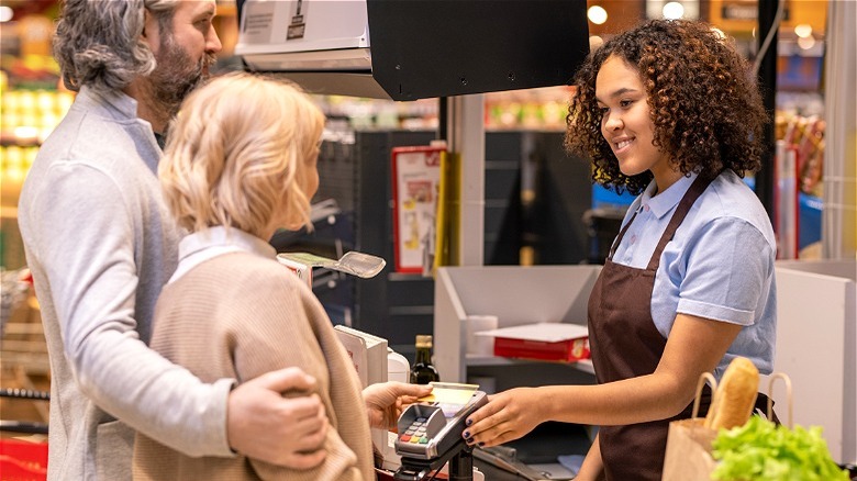 Smiling grocery cashier with customers 