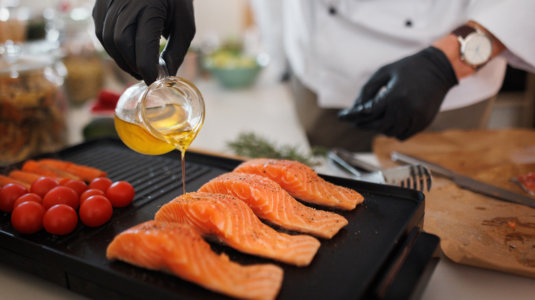 A chef pours olive oil onto four salmon filets