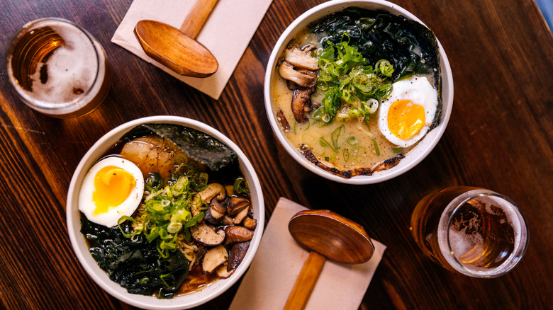 Bowls of ramen topped with boiled eggs and vegetables and beer