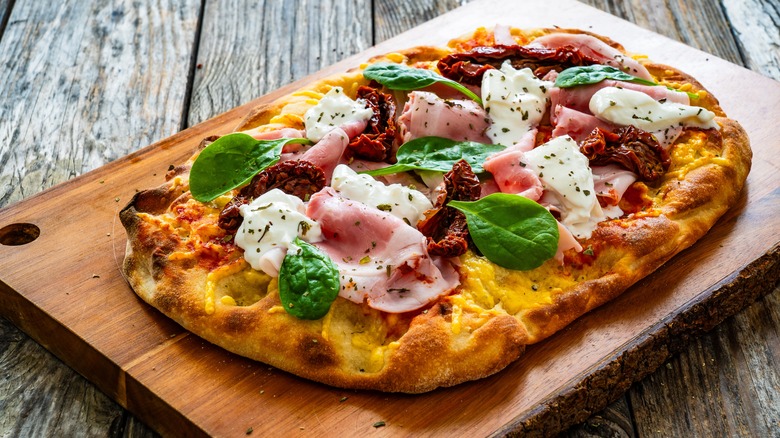 Pizza with sun dried tomatoes, ham, burrata, and fresh basil