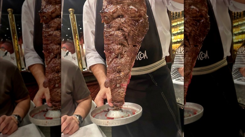 A passadore in a Brazilian steakhouse holds a skewer of fraldinha