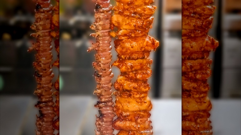 Marinated chicken thighs on a skewer stand next to a skewer of chicken hearts