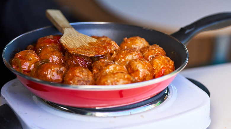 Glazed meatballs cooking on a pan with a wooden spoon on top of it