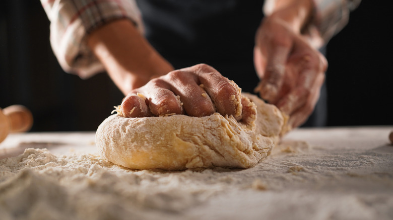 A person making pizza dough from scratch on a floured table