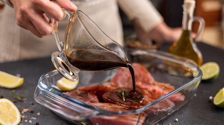 Pouring a marinade on a steak in a glass baking dish